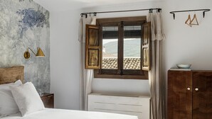A bedroom with a bed, a wooden headboard, a nightstand, a wardrobe, a window with curtains, and a view of a mountain.