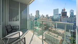 A balcony with a city view, a glass railing, and two black chairs. - Level River North - Spacious Executive Suite (Chicago)