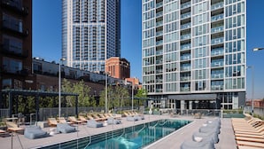 A rooftop pool with lounge chairs and a modern building in the background. - Level River North - Spacious Executive Suite (Chicago)