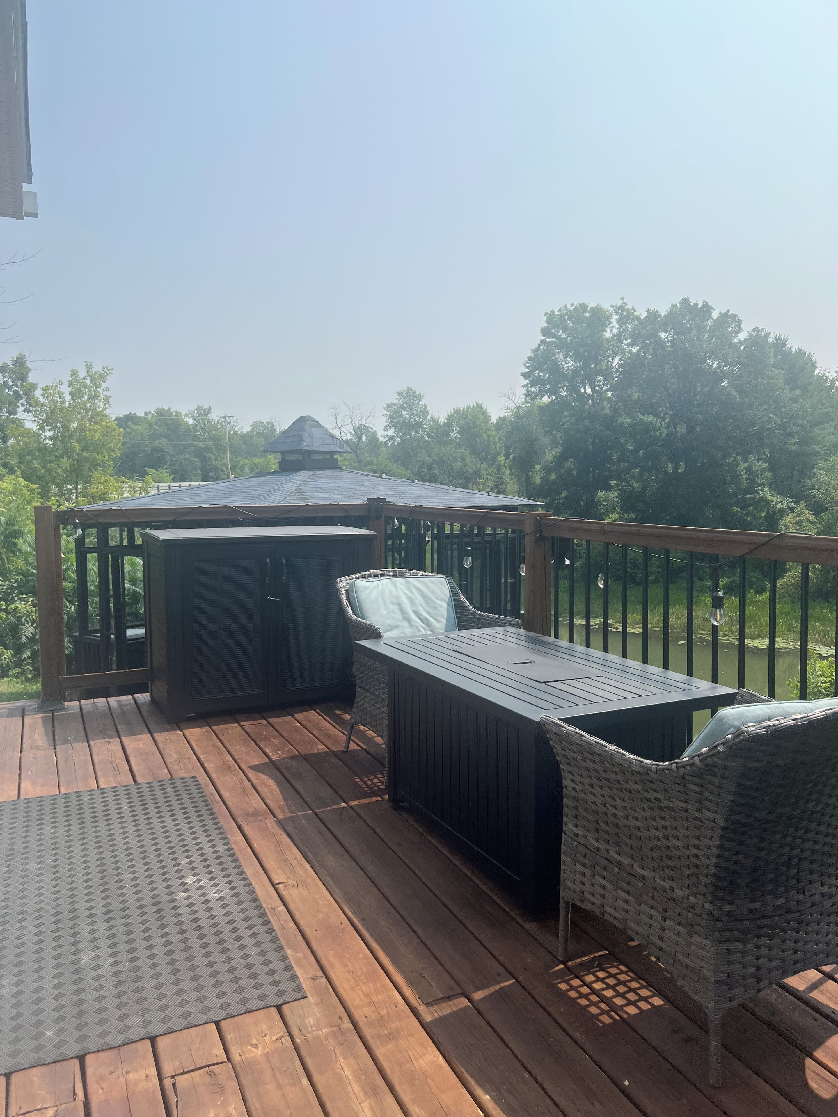Una terraza de madera con mobiliario exterior, incluyendo una mesa y sillas, y un pabellón.