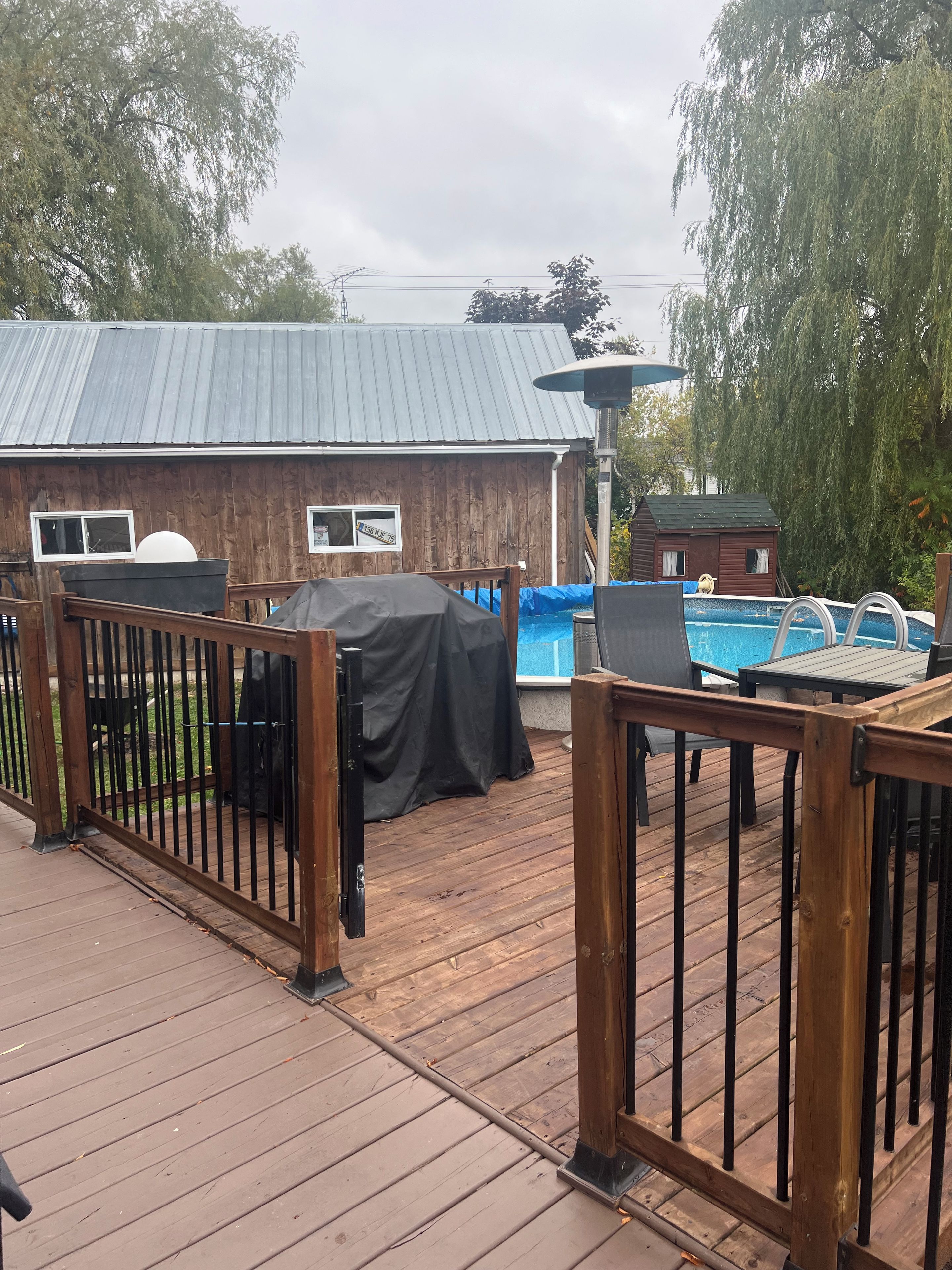 A wooden deck with a pool, a covered grill, and a small shed.