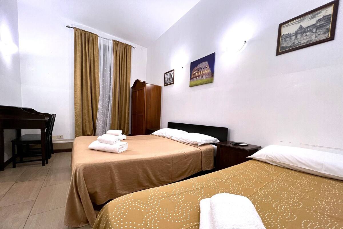 A hotel room with two beds, a desk, and a wardrobe.