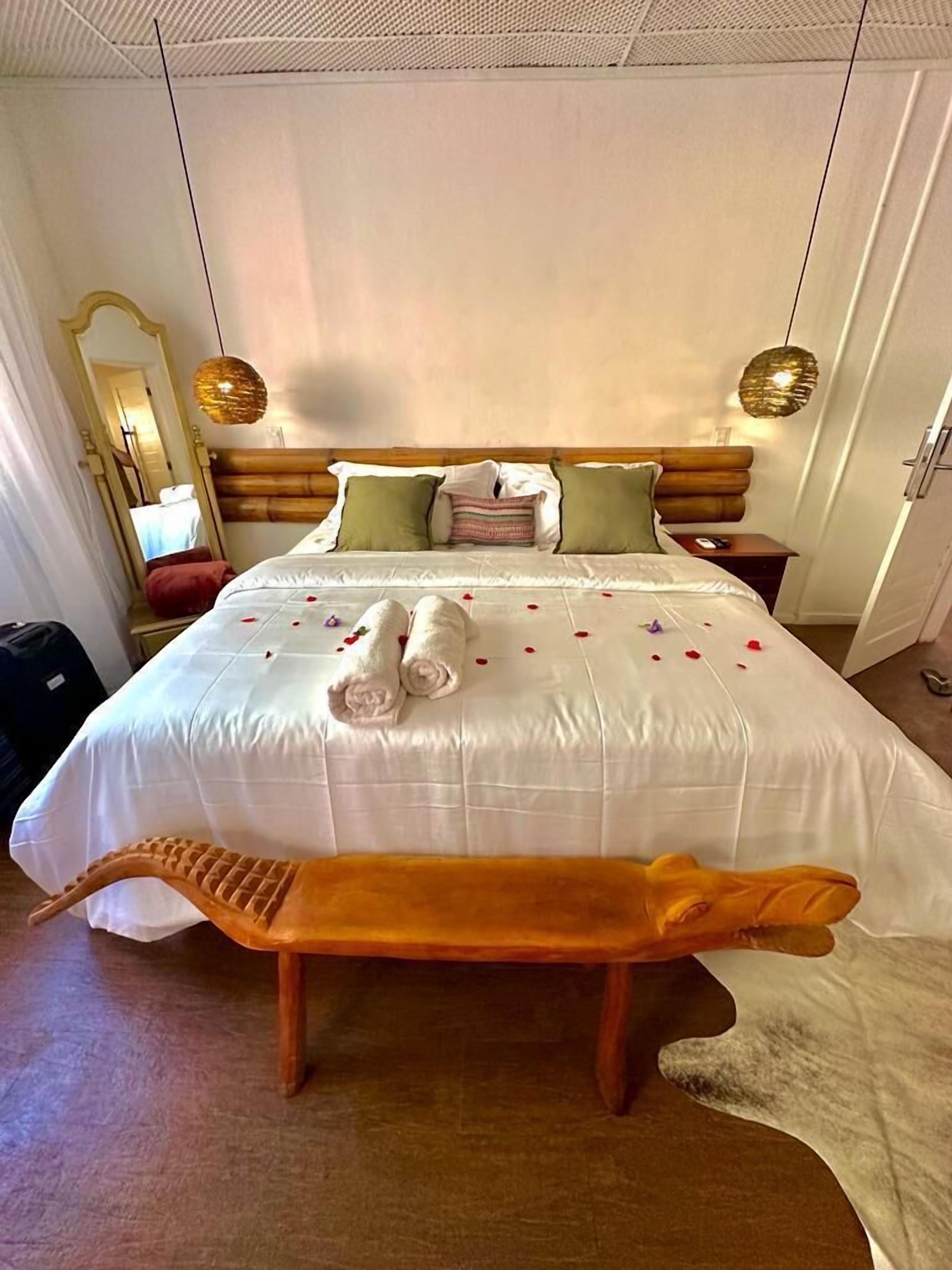 Cama bem arrumada com lençóis brancos, duas almofadas e um banco de madeira na frente.