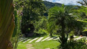 A garden pathway leading to a lush green area with various plants and trees, under a clear blue sky. - Villa Pantai Secret Place (Miracatu)
