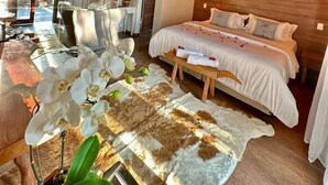 A bedroom with a wooden ceiling, a bed with white bedding, a fur rug, and orchids. - Villa Pantai Secret Place (Miracatu)