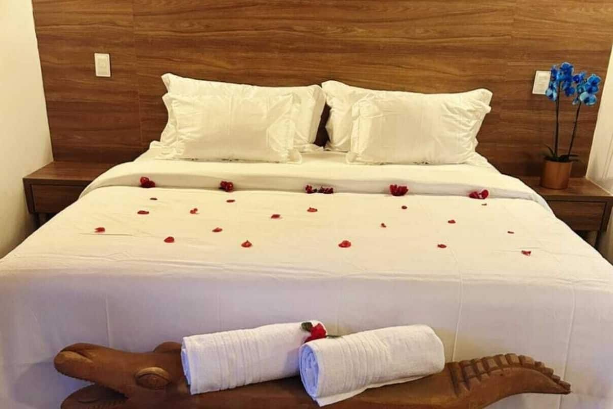Ein Hotelzimmer mit einem hölzernen Kopfteil, einem Bett mit weißen Leinentüchern und roten Rosenblättern, einer Holzbank mit Handtüchern und einem Kuhfellteppich.