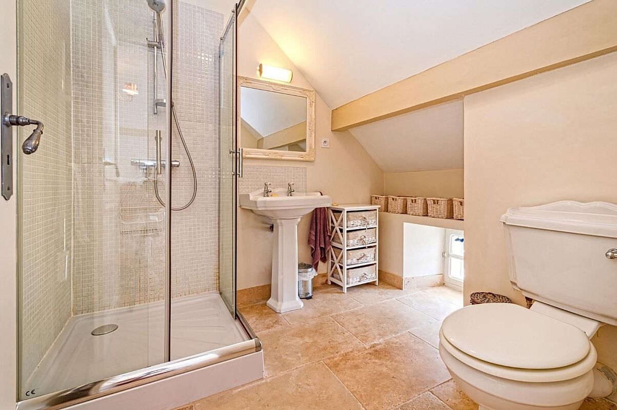 Un baño con ducha de vidrio, lavamanos, inodoro y cestas de mimbre en estantes.
