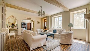 A spacious living room with white sofas, a patterned rug, and a chandelier.