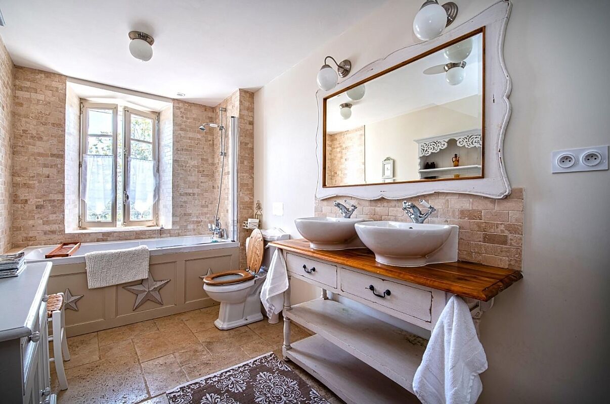 A bathroom with a large window, a bathtub, a toilet, and a vanity with two sinks.