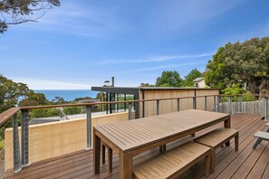 A wooden deck with a table and benches, overlooking a scenic view with trees and a clear sky.