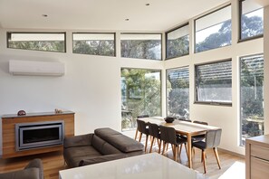 Un intérieur moderne comprenant un coin repas, un canapé, un téléviseur et de grandes fenêtres.