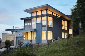Une maison moderne à deux étages, dotée de grandes fenêtres et d’un balcon.