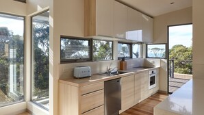 A modern kitchen with wooden cabinets, a stainless steel dishwasher, and a large window overlooking a balcony.