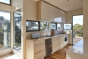 Une cuisine moderne avec des meubles en bois, un lave-vaisselle en acier inoxydable et une grande fenêtre donnant sur un balcon.