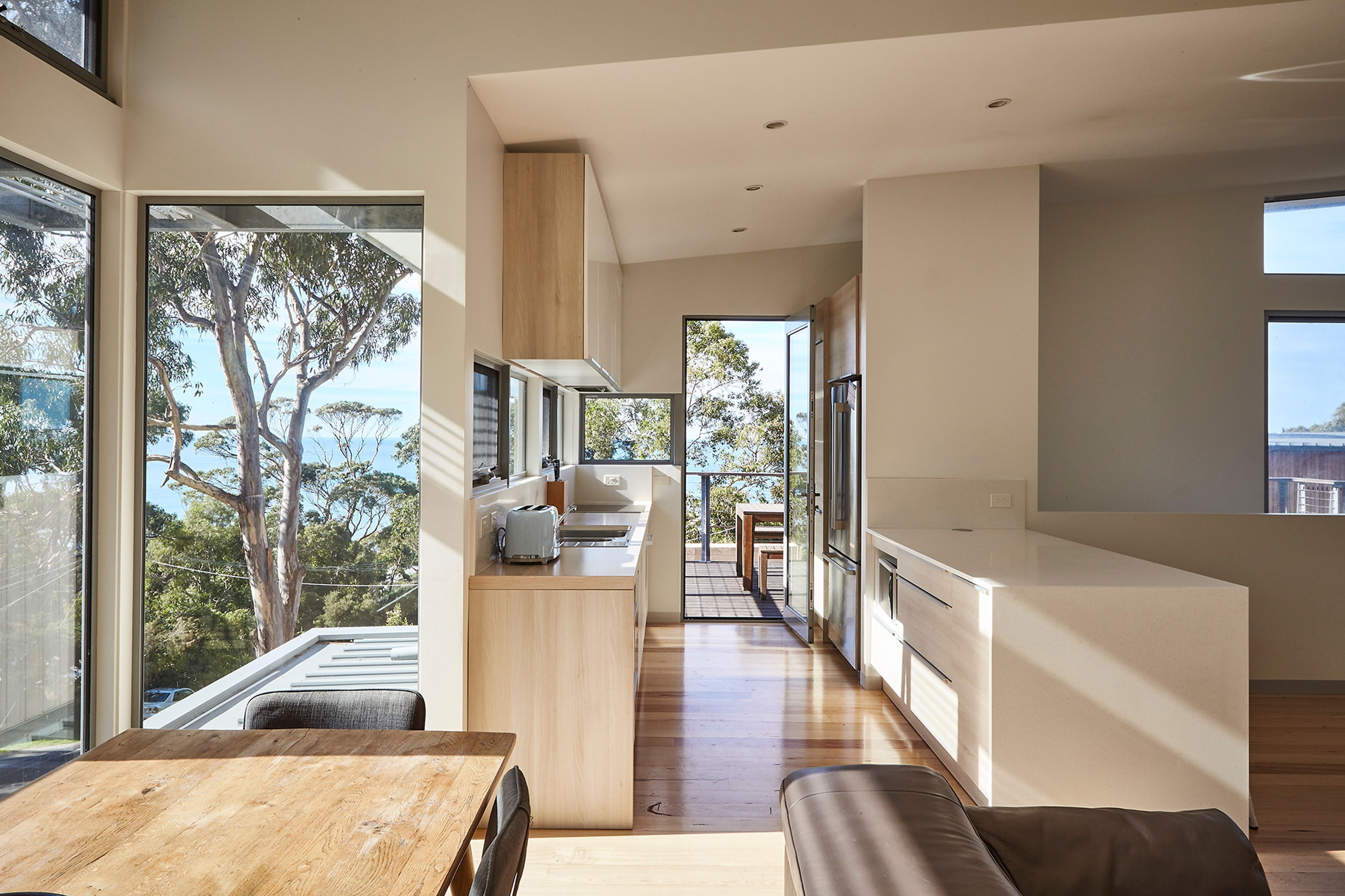 A modern kitchen with a view of the outdoors, a dining area with a wooden table, and a kitchen island.