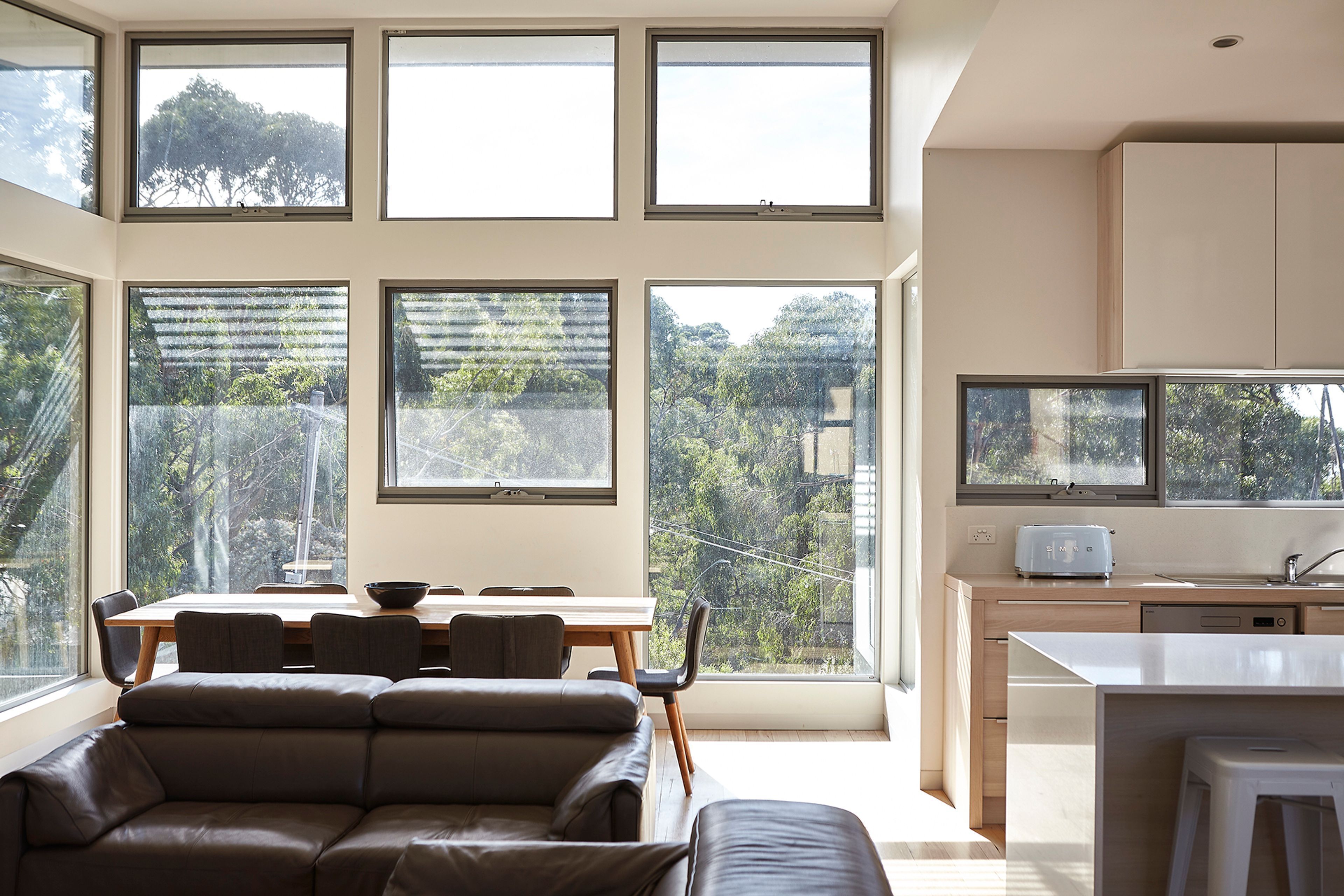 Ein modernes Interieur mit Essbereich, einer Couch, einer Küche und großen Fenstern mit Blick auf Grünflächen.