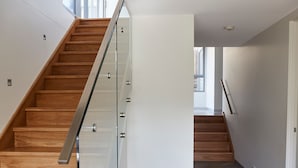 A modern staircase with wooden steps and a glass railing, leading to an upper floor.
