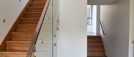 Un escalier moderne avec des marches en bois et une rampe en verre, menant à l’étage supérieur.
