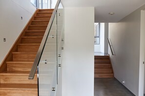 Un escalier moderne avec des marches en bois et une rampe en verre, menant à l’étage supérieur.