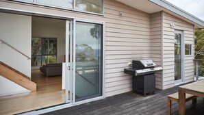 A modern house with a sliding glass door leading to an interior space, a patio with a grill, and a wooden deck.