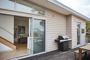 Une maison moderne dotée d’une porte-fenêtre coulissante donnant sur un espace intérieur, d’un patio avec un barbecue et d’une terrasse en bois.