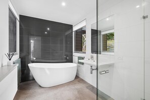 A modern bathroom with a freestanding bathtub, a glass shower enclosure, and a large mirror above the sink.