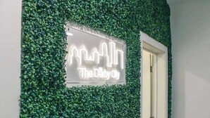 Um sinal com o texto 'The Derby City' ao fundo, vegetação verde.