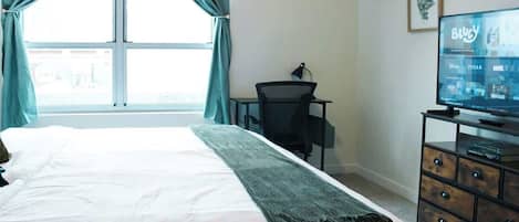 Habitación de hotel con cama, escritorio, televisor mostrando un servicio de streaming y ventana con cortinas.