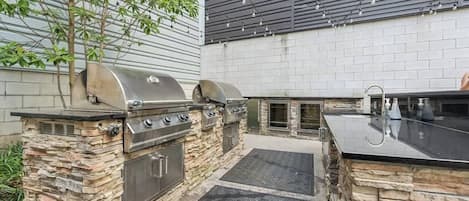 Un espacio de cocina al aire libre con una estación de parilla de piedra, un lavabo y una encimera.