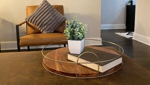 A living room with a brown leather sofa, a round coffee table with a book and a potted plant, and a wall with hanging fabric. - Charming/Cozy/1 Bedroom (Kansas City)