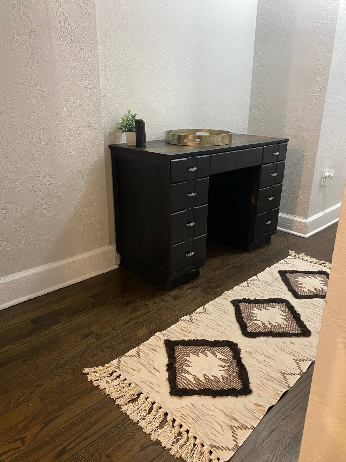 A dark wooden desk with multiple drawers, a small plant, and a brass tray on top.
