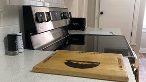 A kitchen with a stainless steel stove, a white tiled backsplash, and a wooden cutting board on the counter. - Charming/Cozy/1 Bedroom (Kansas City)