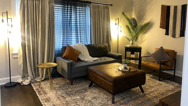 A living room with a sofa, ottoman, and a chair. There is a small table and a lamp. - Charming/Cozy/1 Bedroom (Kansas City)