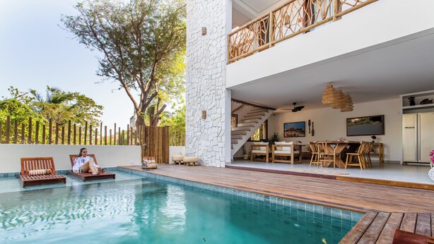 Un espace piscine extérieur moderne, doté d’une terrasse en bois, de chaises longues et d’un escalier menant à un niveau supérieur où se trouve un coin repas.