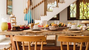 Une table à manger dressée avec différents plats et boissons, des chaises en bois et un escalier en arrière-plan.
