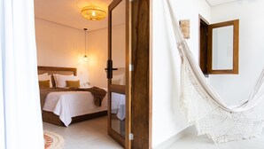 Une chambre avec un lit, une porte en bois, un hamac et un miroir au mur.