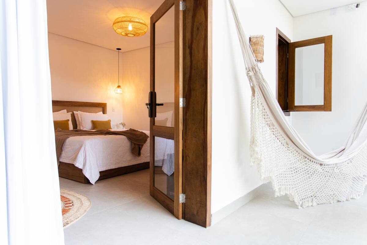 Un dormitorio con una cama, una puerta de madera, una hamaca y un espejo en la pared.