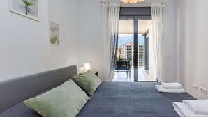 A modern bedroom with a large bed, a balcony with a view of buildings, and a ceiling light fixture. - CALA ALTA beach apartment (Benidorm)
