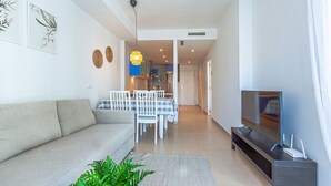 A modern living room with a sofa, a dining area with a table and chairs, a TV, and a kitchen in the background. - CALA ALTA beach apartment (Benidorm)