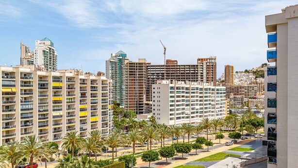 A high-rise residential building with multiple balconies, a rooftop pool, and a view of surrounding urban structures. - CALA ALTA beach apartment (Benidorm)