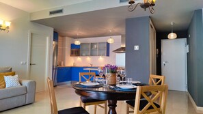 A modern kitchen with blue cabinets, a dining table set for four, and a living area with a sofa and cushions. - CALA ALTA sunrise apartments (Benidorm)