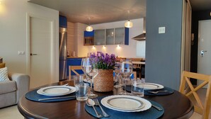 A dining area with a round table set for four, surrounded by chairs. There is a kitchen in the background with modern appliances and cabinets. - CALA ALTA sunrise apartments (Benidorm)