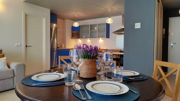 A dining area with a round table set for four, surrounded by chairs. There is a kitchen in the background with modern appliances and cabinets. - CALA ALTA sunrise apartments (Benidorm)