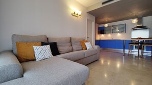 A modern living room with a grey sectional sofa, a kitchen with blue cabinets, and a dining area with a wooden table and chairs. - CALA ALTA sunrise apartments (Benidorm)