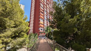 A tall red building with balconies, surrounded by trees and a pathway. - DON MIGUEL blue sky apartment (Benidorm)