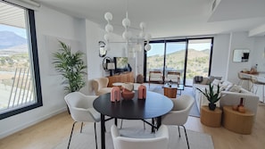 Un salon moderne avec une table de salle à manger ronde, des chaises blanches et une grande fenêtre donnant sur le paysage.