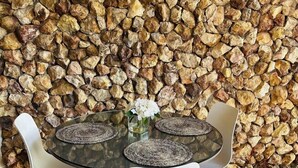 A round glass table with four white chairs, set against a backdrop of a stone wall. - Romantic and cozy apartment in tropical villa w/ mountain and flowers view.  (Altos del Maria)