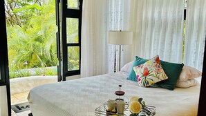 A spacious bedroom with a large bed, a ceiling fan, and a view of lush greenery outside. - Romantic and cozy apartment in tropical villa w/ mountain and flowers view.  (Altos del Maria)