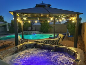 Ett bubbelbad med ett lusthus ovanför, omgivet av solstolar och en swimmingpool.