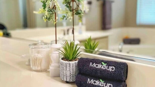 Et badeværelse med et spejl, en vask, en lille potteplante, et glas og to håndklæder med ordet "Makeup".